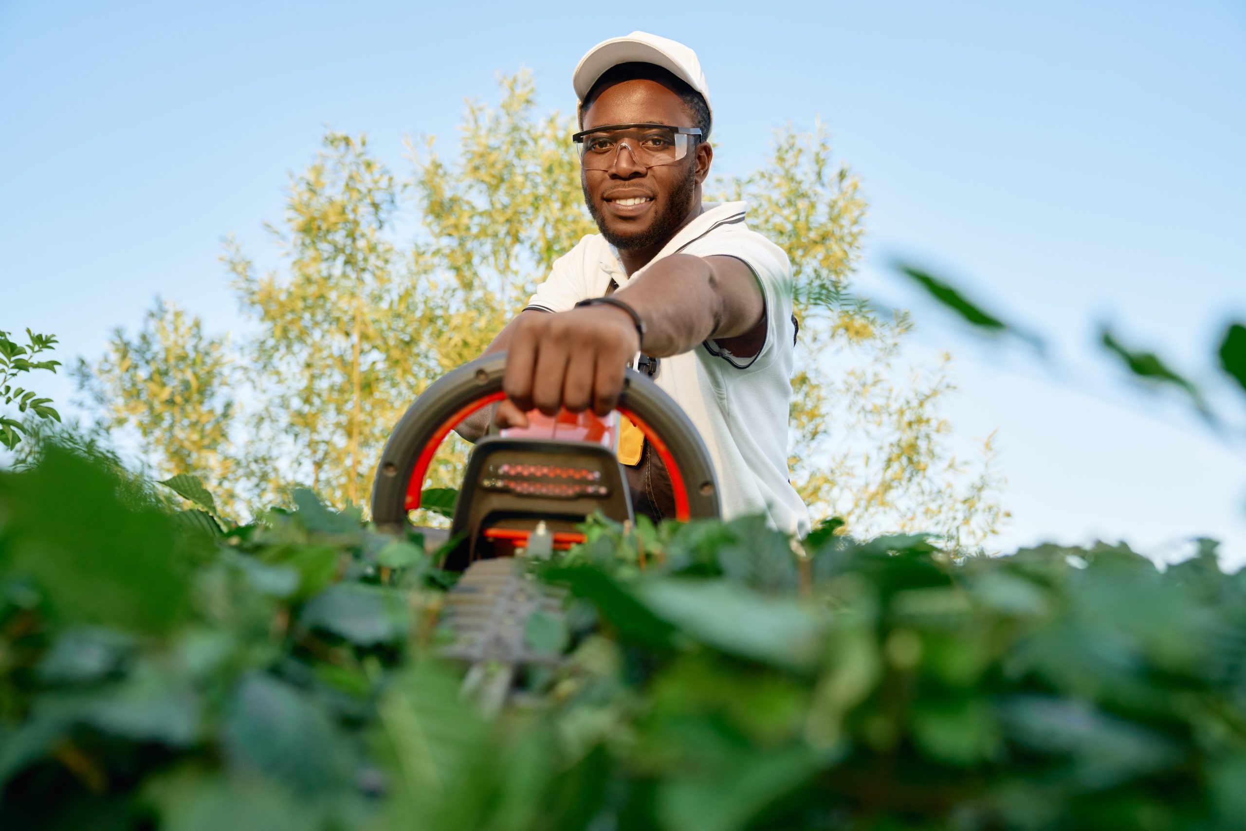 portrait cheerful african man pruning hedge with trimmer min